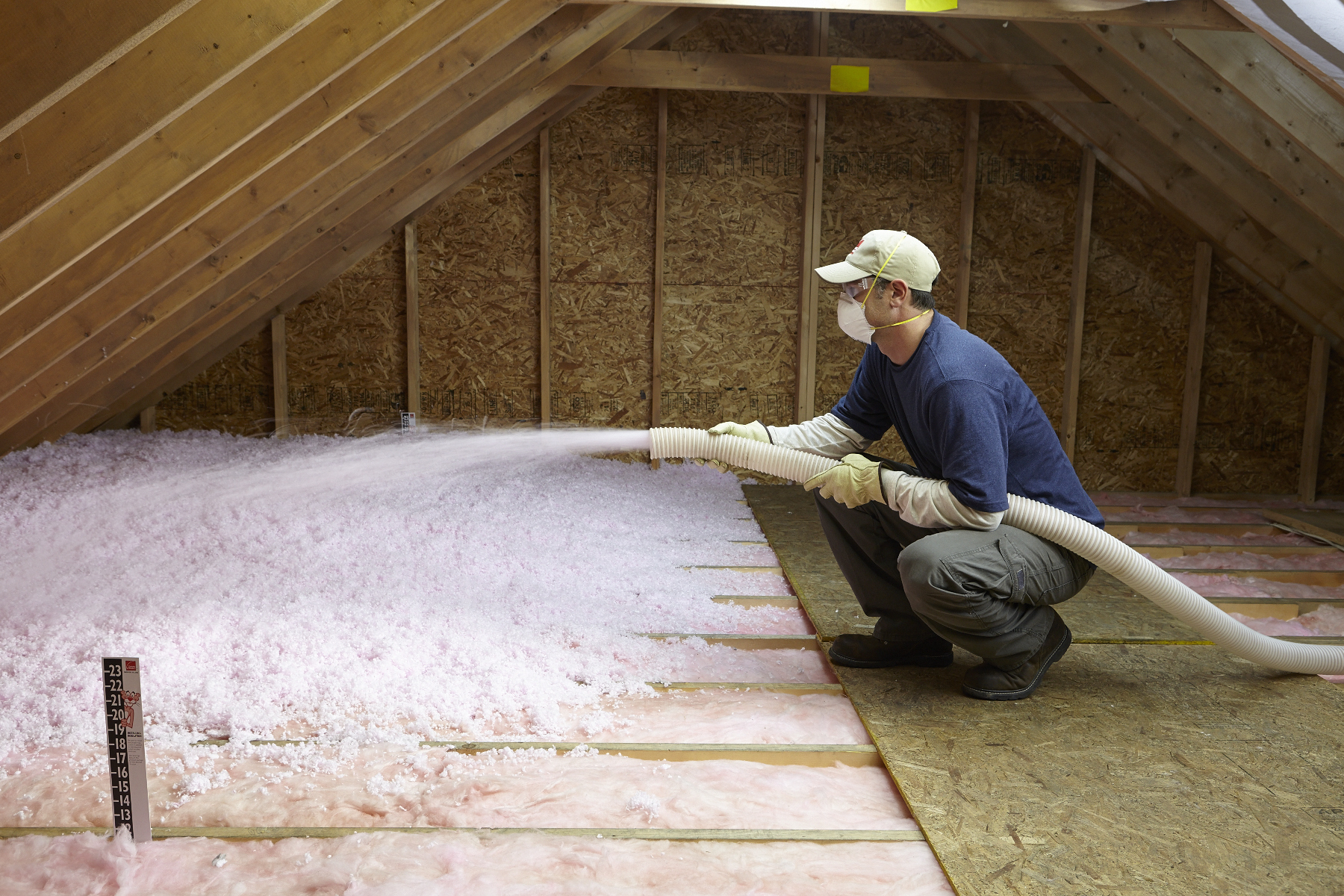 photo of blown-in fiberglass insulation being installed over batt fiberglass insulation in an attic